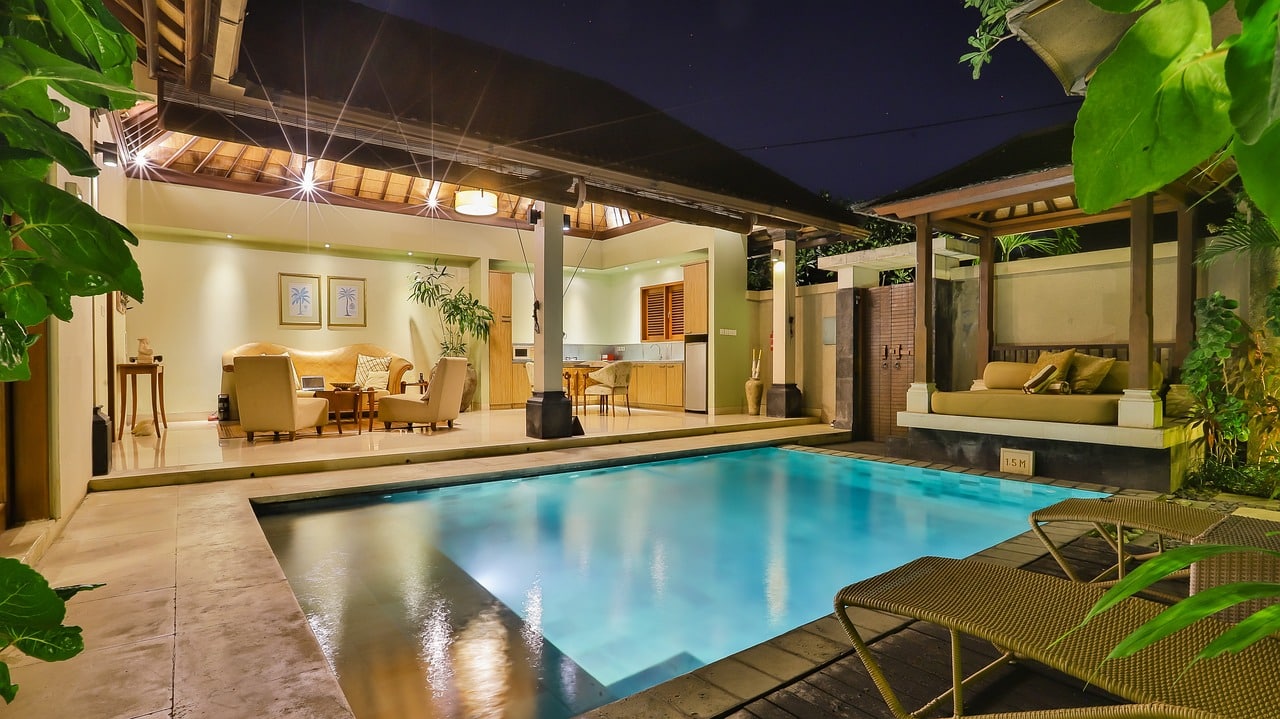 An illuminated pool and patio area at night, showcasing a dining area, creating a serene and inviting atmosphere.