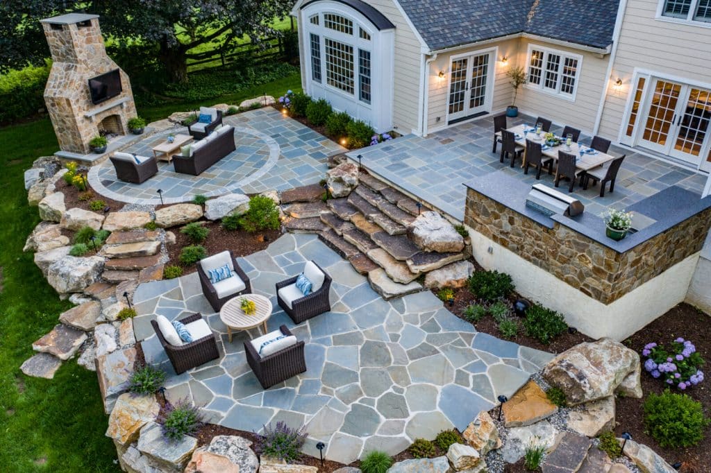 Spacious outdoor patio with seating areas, dining table, and stone fireplace.