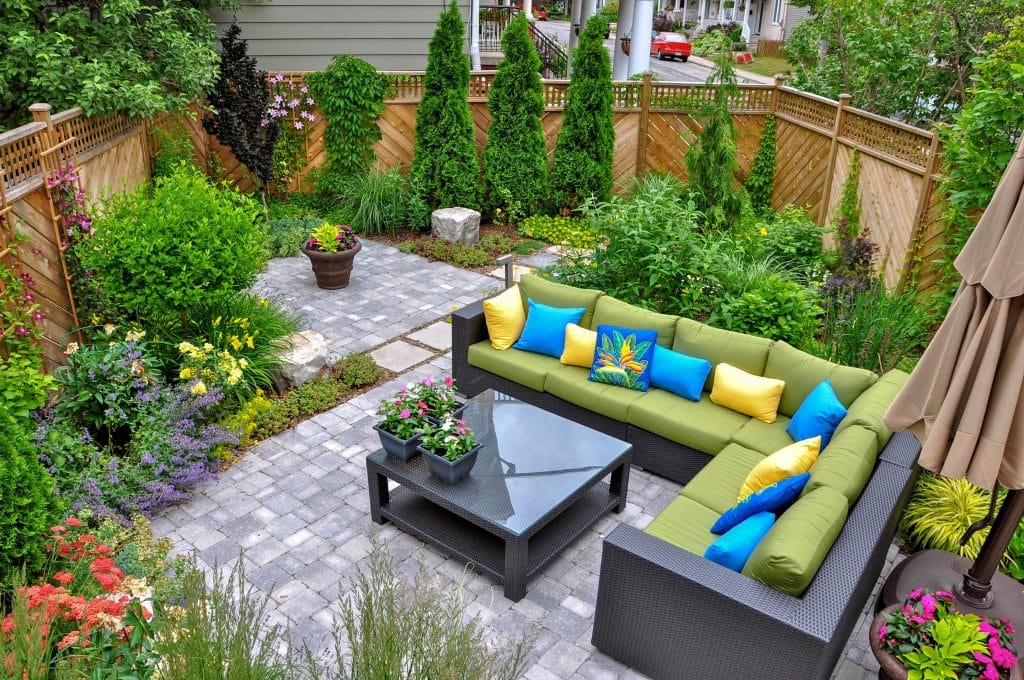 Cozy patio with green and blue cushioned seating, surrounded by lush plants.