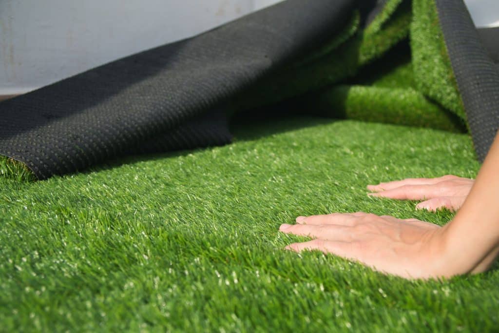 Hands installing a roll of artificial grass on the ground.