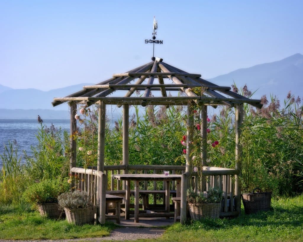 Open wooden gazebo by lake with mountain backdrop