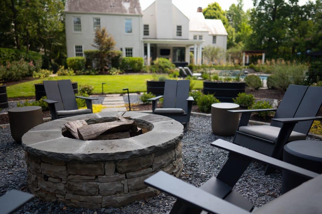 Stone fire pit with landscape lighting and modern chairs.