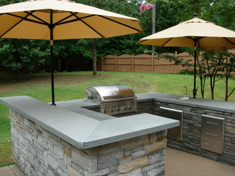 Stone outdoor kitchen with grill and umbrellas.