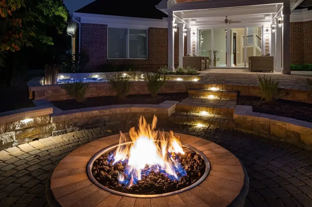 Hidden LED lighting recessed under a stone retaining wall cap and stone steps for a clean line of light on a paved patio.
