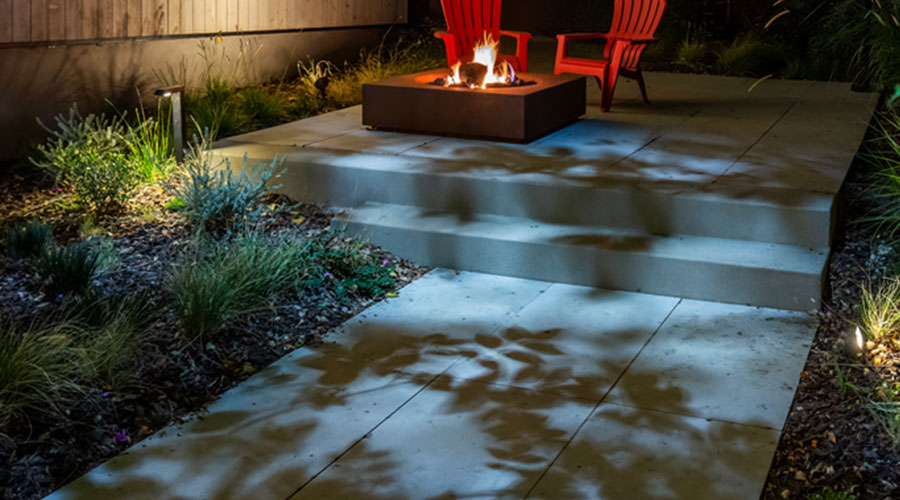 Moonlighting landscape lighting idea casting cool dappled light on cement patio around a firepit